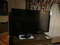 Front view of black flat screen television on a stand with remote and manual on the surface.