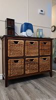 Front view of wood frame chest with six wicker baskets as drawers. Dark wood framing with woven wicker baskets, two rows of three drawings.
