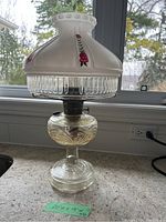 Front and side view of Aladdin hurricane oil lamp showing the clear textured glass base, metal burner, and hand-painted frosted glass shade with red roses.