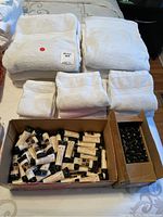 Two boxes with many small tubes of AMBR Green Tea Spa lotion and folded white towels (bath, hand, washcloth) arranged on a surface.
