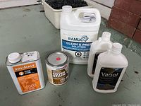 Photo showing all four items together: two bottles of Varsol (one half full), a full jug of Ramuc Clean & Prep Solution, a 3/4 full can of Zinsser Cover Stain Paint, and 1/4 full can of Solvable Xylene solvent.