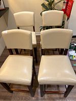 Four beige pleather cushioned bar stools with brown wooden frames arranged closely together showing backs and seats