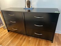 Front view showing six drawers, black finish, metal handles, minor wear.