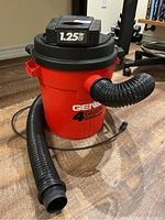 Front view of red Genie wet/dry vacuum showing hose attached and power cord on floor.