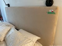 Full view of the beige velvet or suede-covered king size headboard attached to a bed, showing size and design.