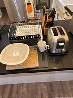 Full view of kitchen items on countertop including toaster, dish rack, cutting boards, mug, bowl, and wooden knife block.