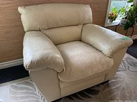 Front angle photo of large cream leather arm chair with cushioned seat covered by beige protective fabric cover, showing padded arms and backrest.