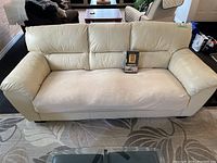 Front view of cream leather couch with protective mesh seat cover and unopened furniture care kit box placed on seat.