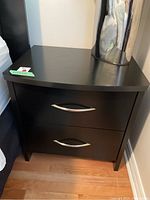 Front view of dark wood nightstand with two drawers and metal handles, showing overall condition and style.
