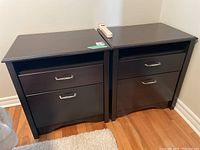 Pair of dark wood nightstands placed side by side on a hardwood floor, showing front elevation with two drawers and open shelf each.
