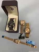 Four watches displayed: U.S. Polo Assn. men's watch in box with black and gold band; two gold-tone ladies' watches; Bosch Oyster Perpetual men's watch gold tone.