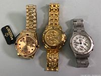 Three watches displayed: REGINALD gold-tone with crystals and pink jewel hour markers, gold-tone Caesium chronograph, silver GUESS Waterpro 50m chronograph watch.