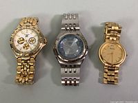 Photo of three watches side by side: gold-tone Bulova ladies watch, gold-tone Fossil men's chronograph watch, and silver-tone Guess men's watch.