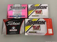 Four boxes of golf balls: one Titleist Pro V1x and three Srixon Z-Star Tour Yellow, unopened but open boxes.
