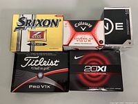 Five boxes of new golf balls from Titleist, Srixon, Callaway, and Nike displayed showing the closed boxes and branding.