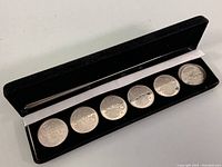 Full view of black velvet-lined box with six silver coins inside, each embossed with 'Animal Skins' and golf clubs.