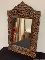 Angled photo showing full mirror with elaborate leaf and floral carved wooden frame in medium brown wood finish.