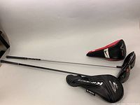 Two golf drivers laid flat with their respective head covers: one Cobra KING F7 and one Nike VRs.