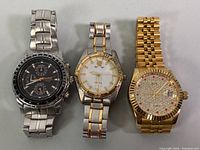 Three wristwatches side-by-side: Men's Casio chronograph with black dial and silver band; ladies Fossil two-tone silver/gold watch with white dial; ladies BOS Angela gold-tone watch with rhinestone-encrusted dial and red gem markers.