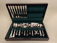 Full view of the wooden chest with the flatware arranged inside, showing forks, spoons, knives, and assorted utensils on green felt.