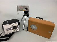 Photo showing Casio Exilim EX-Z40 silver digital camera with 4.0 MP and Pentax lens, alongside Mercury Slim digital camera on tripod, and a tan leather case radio.