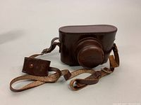 Brown leather carrying case for vintage Regula K camera, with attached strap and lens hood cover.