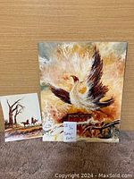 Photo of two paintings, one large with a bird and flames, one smaller with riders and trees