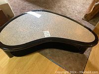 Top view of kidney-shaped coffee table showing textured glass top and wood frame.