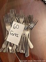 Photo of 40 stainless steel forks arranged on a surface, with a piece of paper indicating '60 Forks'.