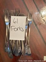 Twenty metal forks arranged together with a paper note indicating '61 Forks' sitting on a wooden surface.