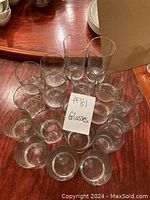 View of 20 clear glasses varying in height and size arranged on a wooden surface with a card labelled '#81 Glasses'.