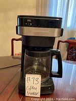 Front view of Hamilton Beach coffee maker showing glass carafe with measurement markings and brand label.