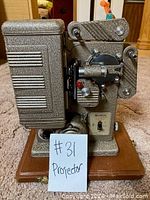 Side view of Keystone Eighty 8mm film projector with metal body and wooden base, showing adjustment knobs and lens assembly.