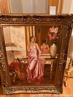 Full view of the large framed oil painting showing a woman in a pink gown standing beside a table with guitar and floral vase.