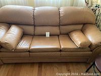 Front view of tan leather three-seat couch with cushioned seats and armrests.