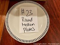 Top view of a single round dinner plate showing white surface with black striped rim and a label reading '#23 Round Medium Plates'
