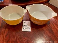 Two yellow Pyrex mixing bowls with white interiors and floral patterns, placed on a wooden surface with a note indicating #9 Pyrex Bowls.