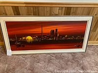 Framed painting of Toronto skyline on carpet floor showing full size, colors, and frame detail.