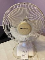 Front view of white Westinghouse table fan showing circular metal grille, three plastic blades, and logo on center hub.