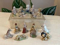 Photo of 15 vintage porcelain Red Rose Whimsies figurines displayed on and around a clear box, showing detailed hand-painted animal and human figures.