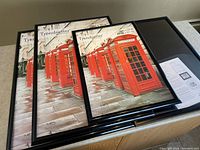 Four new Trendsetter poster frames in black gloss plastic. Frames are shown together on a flat surface with placeholder prints featuring red British telephone boxes.