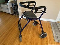 Metal frame adult mobility walker in metallic blue with black cushioned handles, foldable seat, and hand brakes on handles. Front wheels are large and swivel, rear legs have rubber tips.