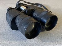 Front angled view of black textured Optiramic binoculars showing large eyepieces and focus adjustment knob.