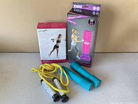Home fitness equipment items including the boxed Pilates resistance tubing, boxed inflatable boxing tower, blue dumbbells, and weighted jump rope.