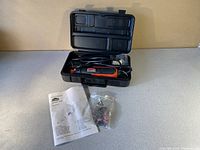 Jobmate rotary tool inside black carrying case with power cord visible, owner's manual and attachments in plastic bag placed outside case on table