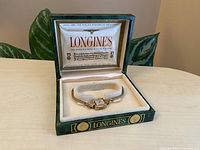 Vintage Longines ladies wristwatch displayed in original green leather-textured box with cream velvet lining.