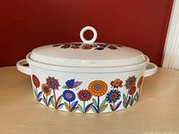 Front view of the oval ceramic lidded casserole dish showing colorful flower and butterfly decorations along the side and lid.