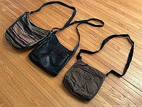 All three crossbody bags laid flat on hardwood floor - woven, black leather, and brown nylon