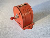 Side angle showing the red metal casing with hand crank and rope clothing line exit point at the top.