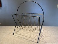 Front and top view of the vintage wire magazine rack showing round handle and zigzag wire slots for magazines.